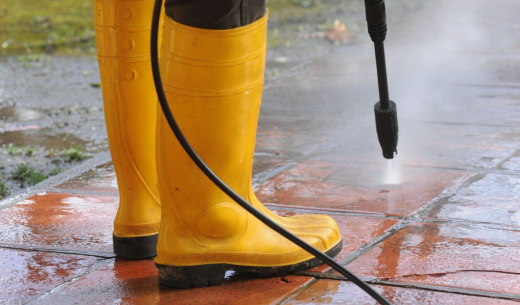 person wearing yellow rubber boots with high pressure water nozzle cleaning dirt tiles
