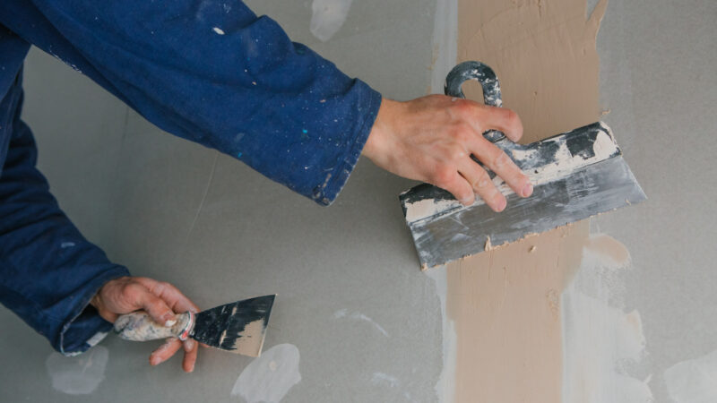 plasterer-man-works-plastering-two-trowels-plasterboard-blue-uniform